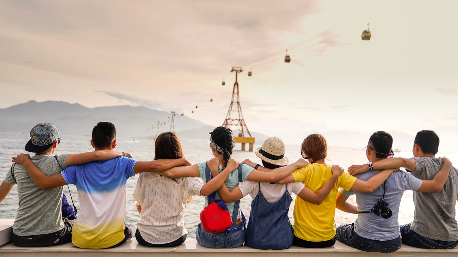 Groupe d’amis bras dessus bras dessous, vue sur la mer au coucher du soleil